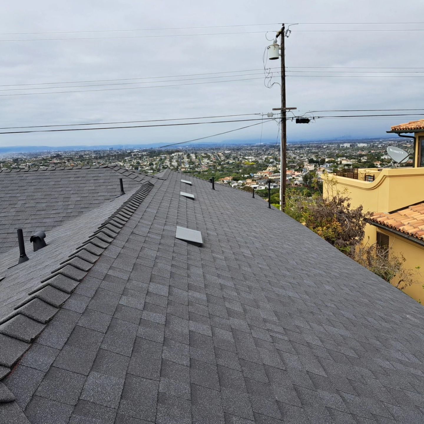 Rooftop with gray shingles overlooking a coastal neighborhood and ocean under a clear sky