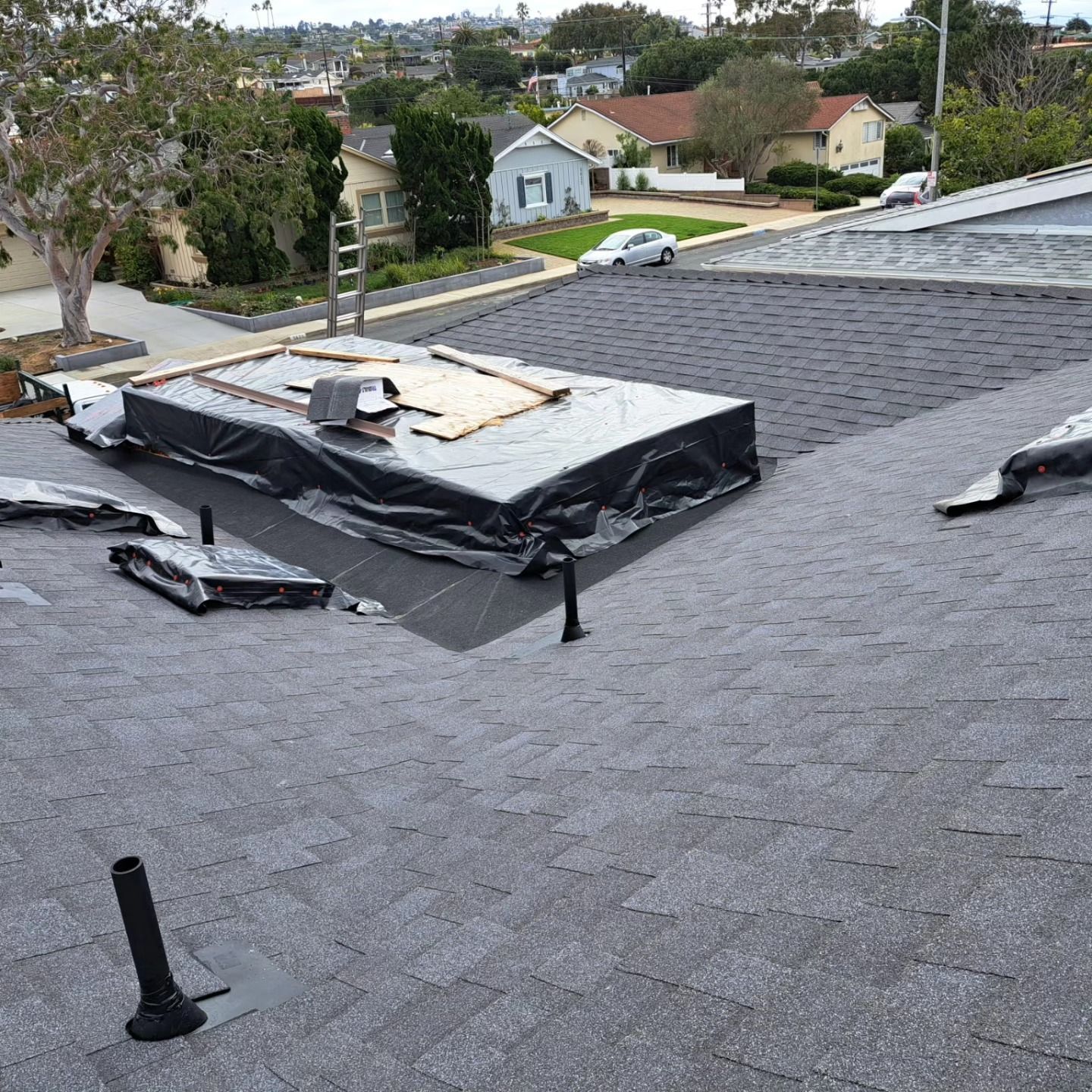 Rooftop with black tarps covering a damaged section, gray shingles, and a suburban neighborhood in the background