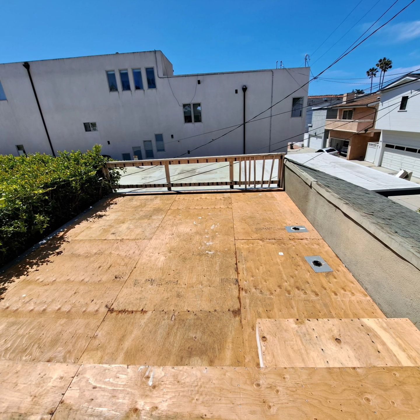 Rooftop plywood deck under construction beside white buildings on a sunny day