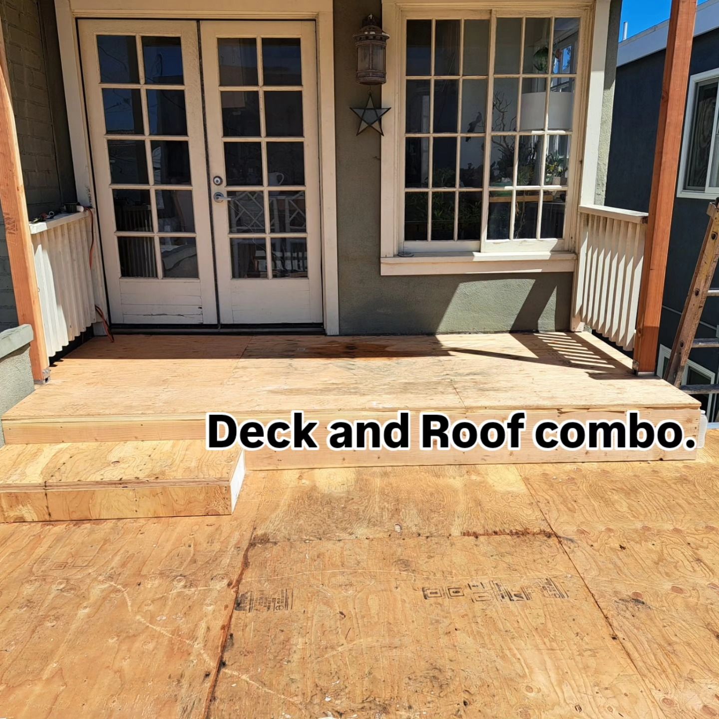 Wooden deck under construction in front of double doors and a window on a porch