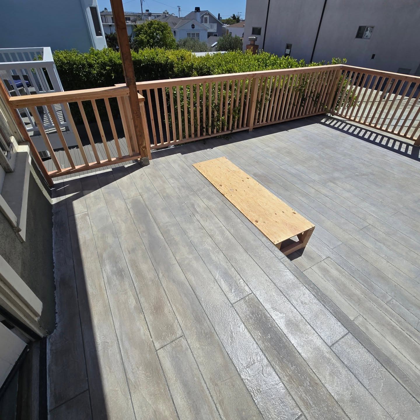 Rooftop deck with gray wood flooring, railing, and a small plywood board in the center.