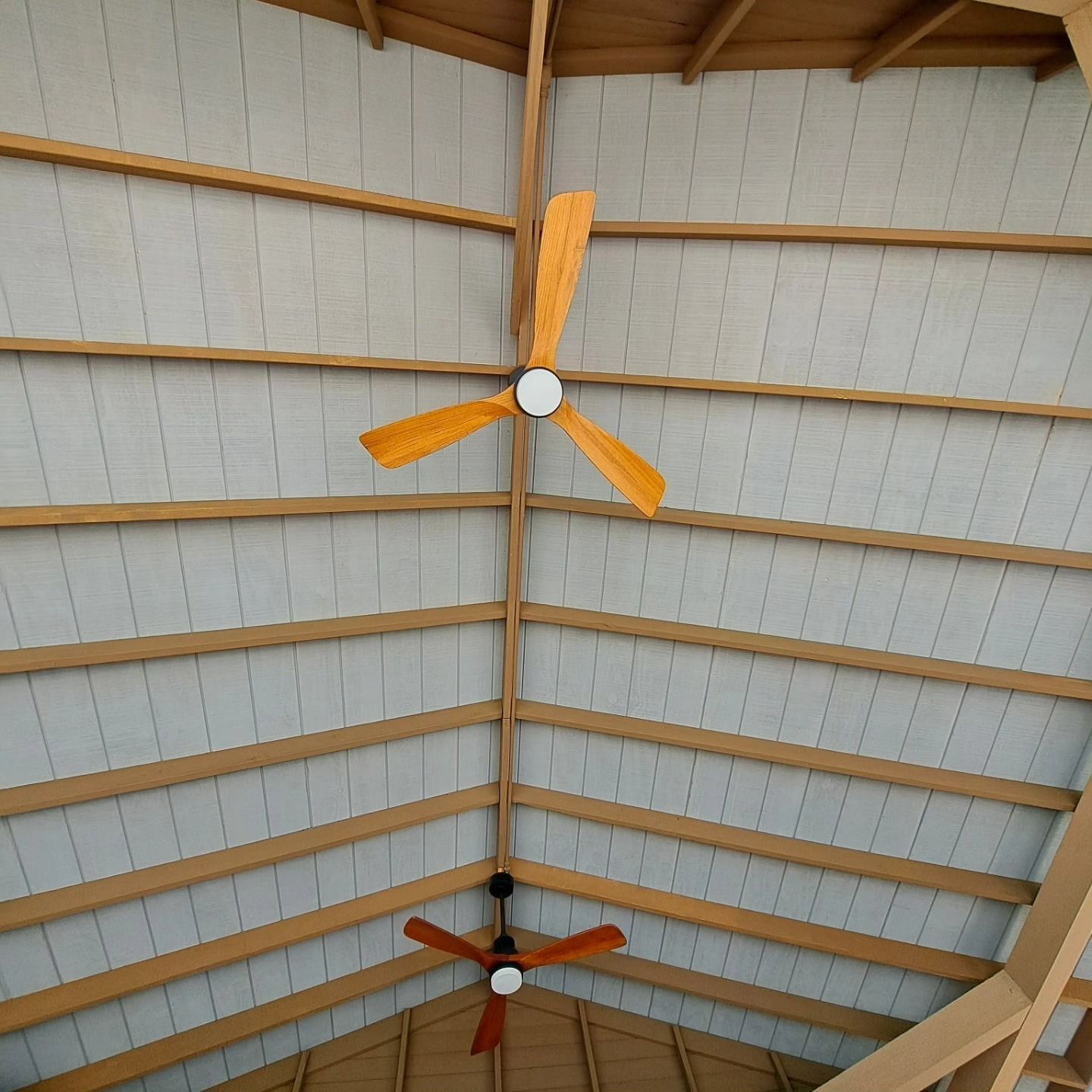 Ceiling with two orange three-blade fans under a vaulted metal roof