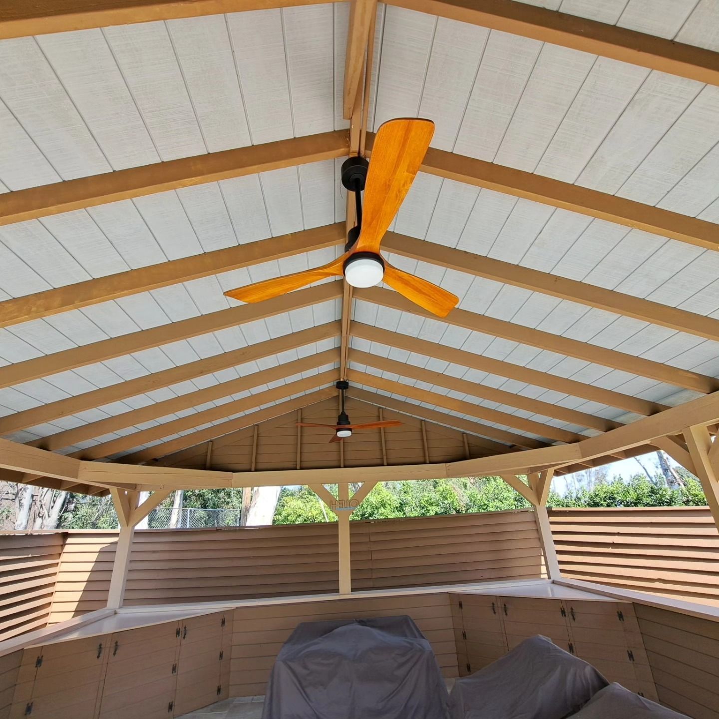 Covered patio ceiling with a yellow ceiling fan and wood beams above outdoor furniture