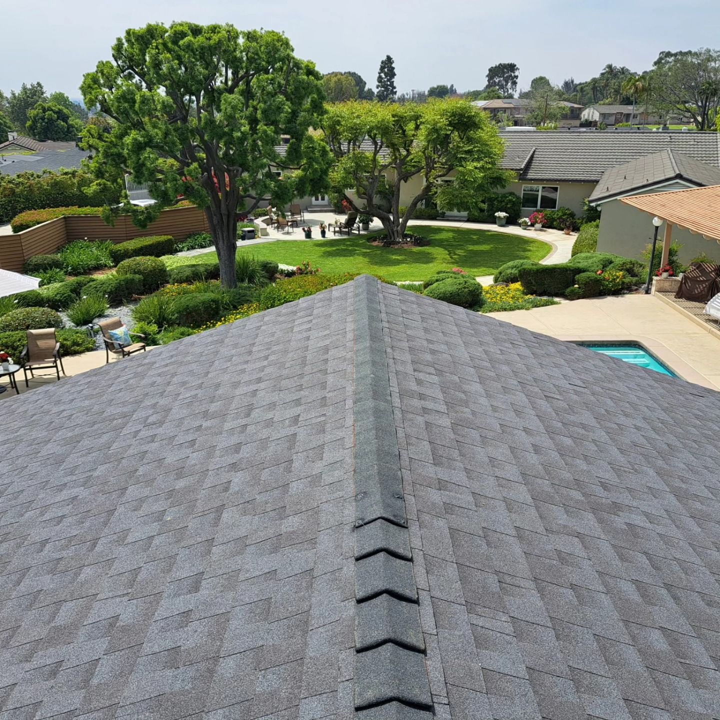 View from a rooftop over a landscaped suburban yard with trees, patios, and a pool