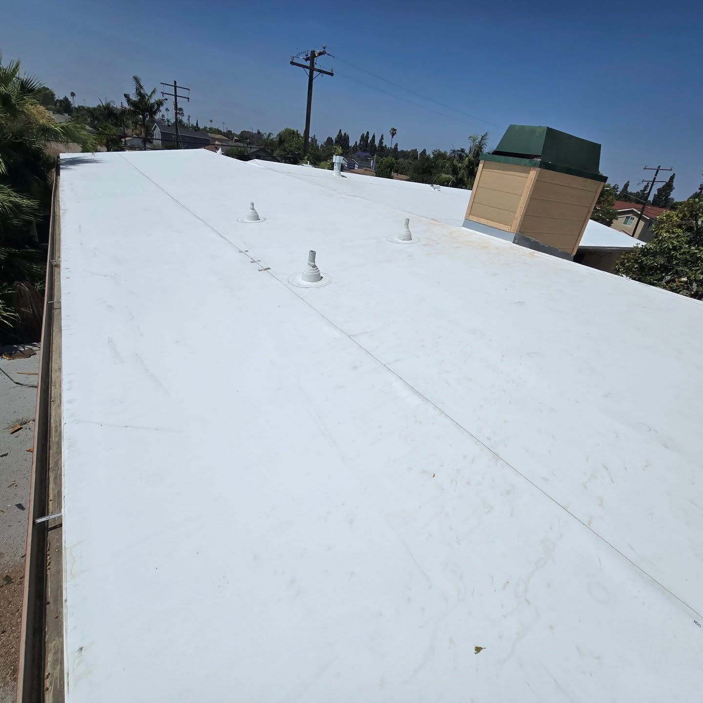 White rooftop with vents and a small brick structure under a clear blue sky