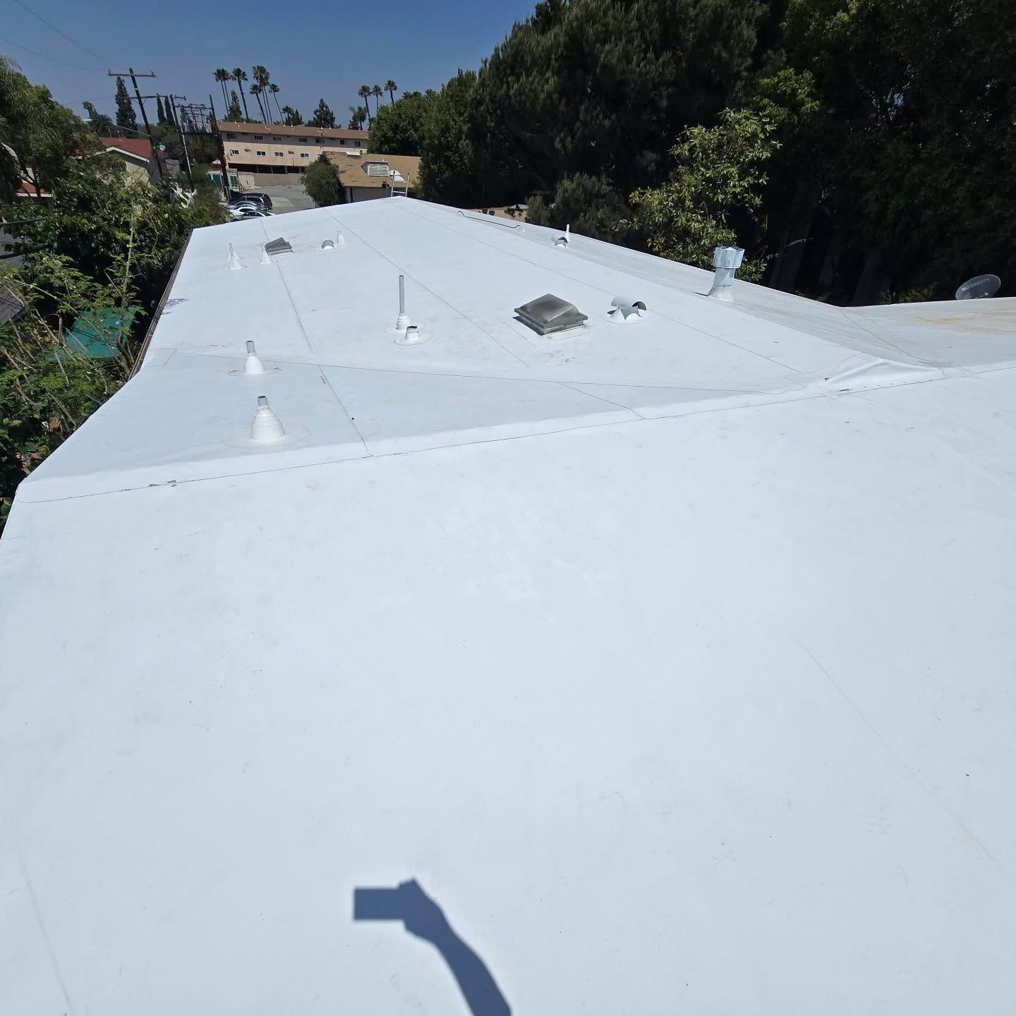 White flat rooftop with vents, skylight, and trees in the background under bright sunlight