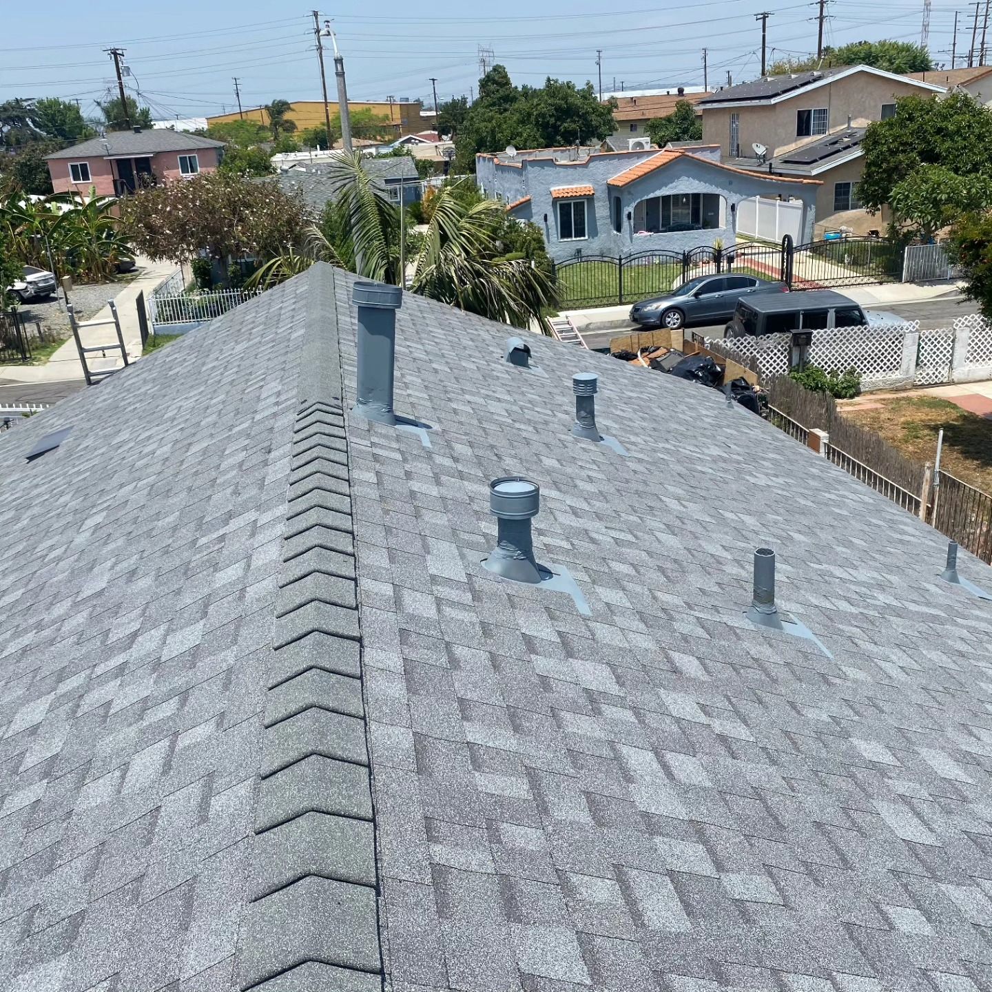 Gray shingled rooftop with vents, overlooking a suburban neighborhood on a sunny day