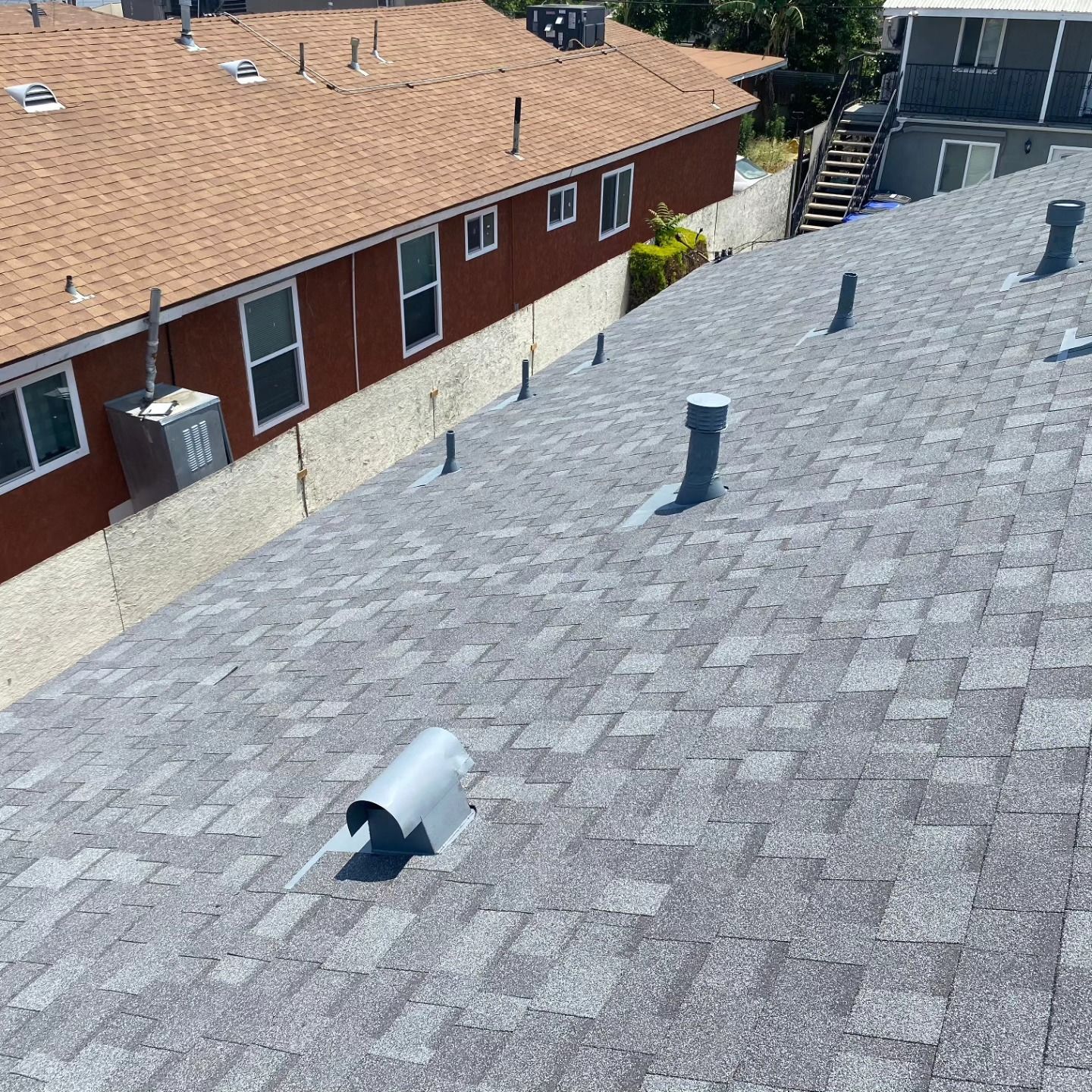 Rooftop view with gray shingles, several vent pipes, and neighboring houses in the background