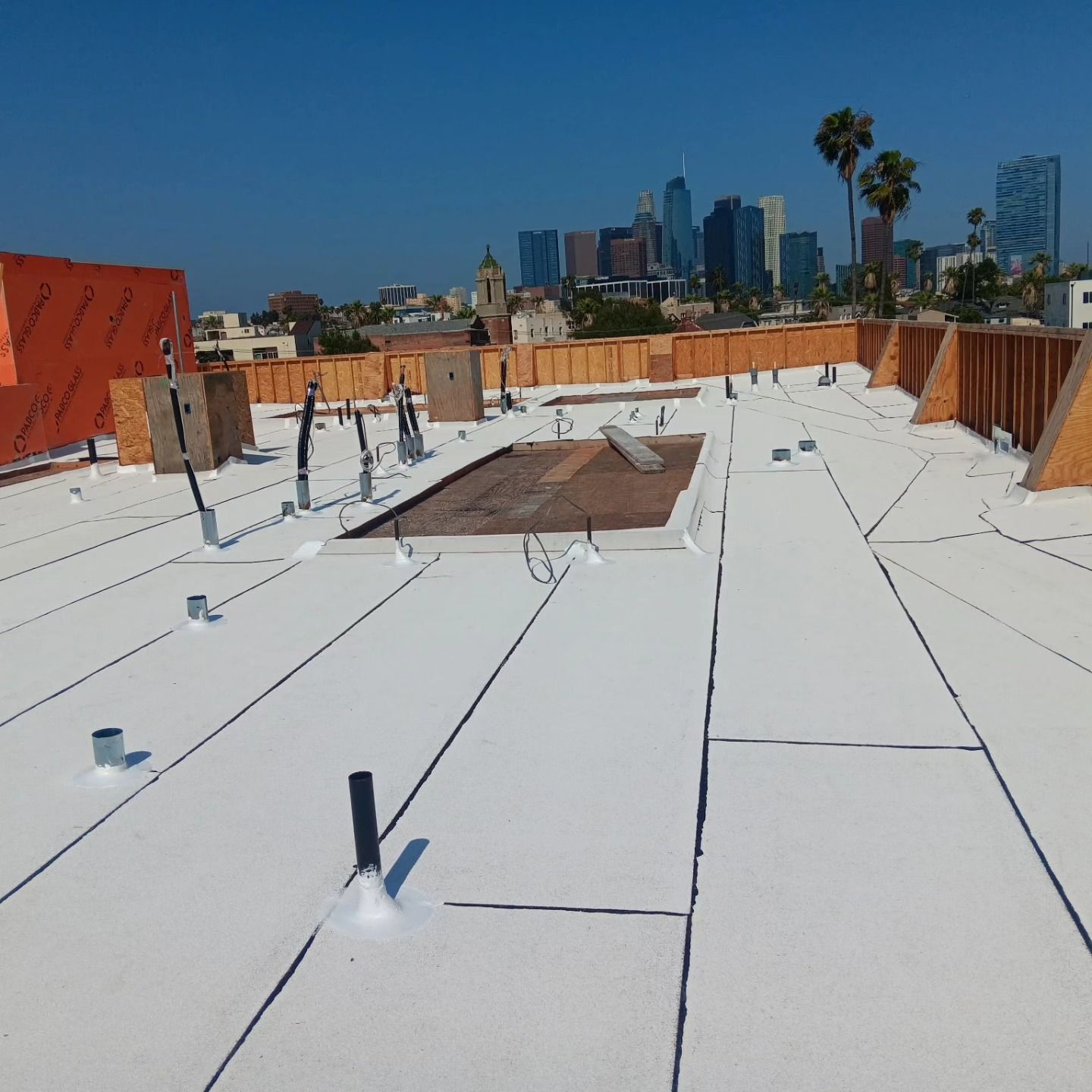 White rooftop with HVAC vents and city skyline under a clear blue sky
