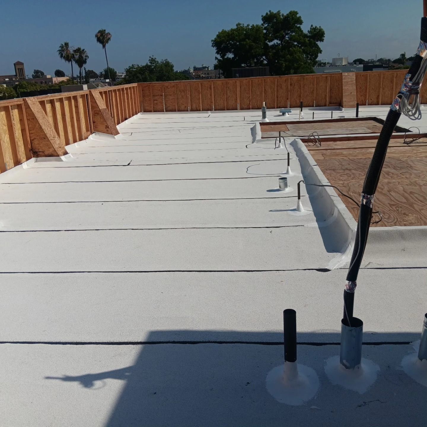 Flat white rooftop under construction with parapet walls, pipes, and a clear blue sky.