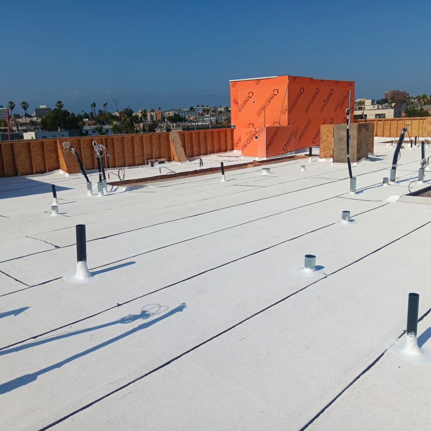 White flat rooftop with pipes and orange equipment box under a clear blue sky