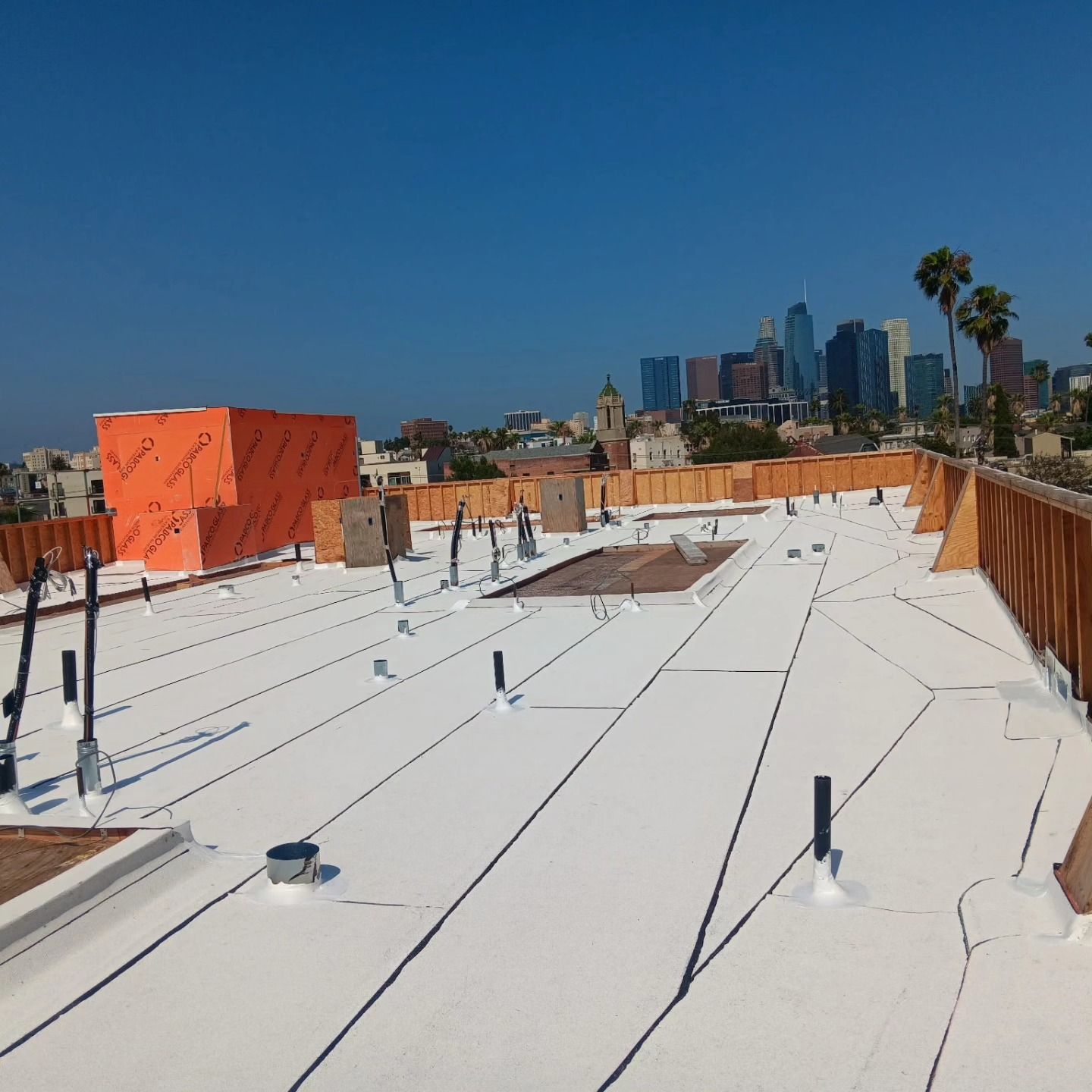 Rooftop with white membrane surface, orange structures, and a city skyline under a clear blue sky.