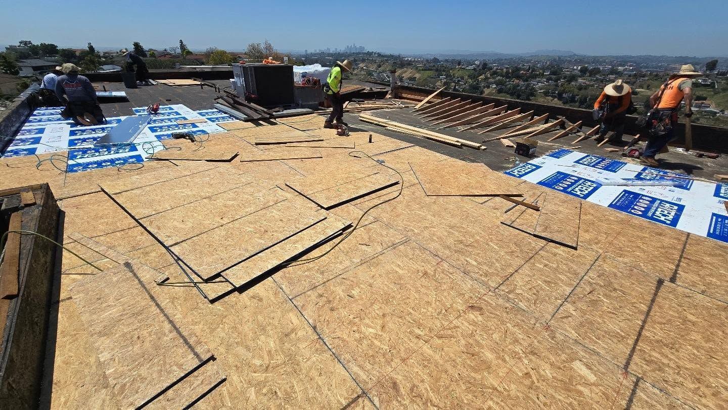 Roofing crew installing plywood sheathing and blue underlayment on a house roof in progress