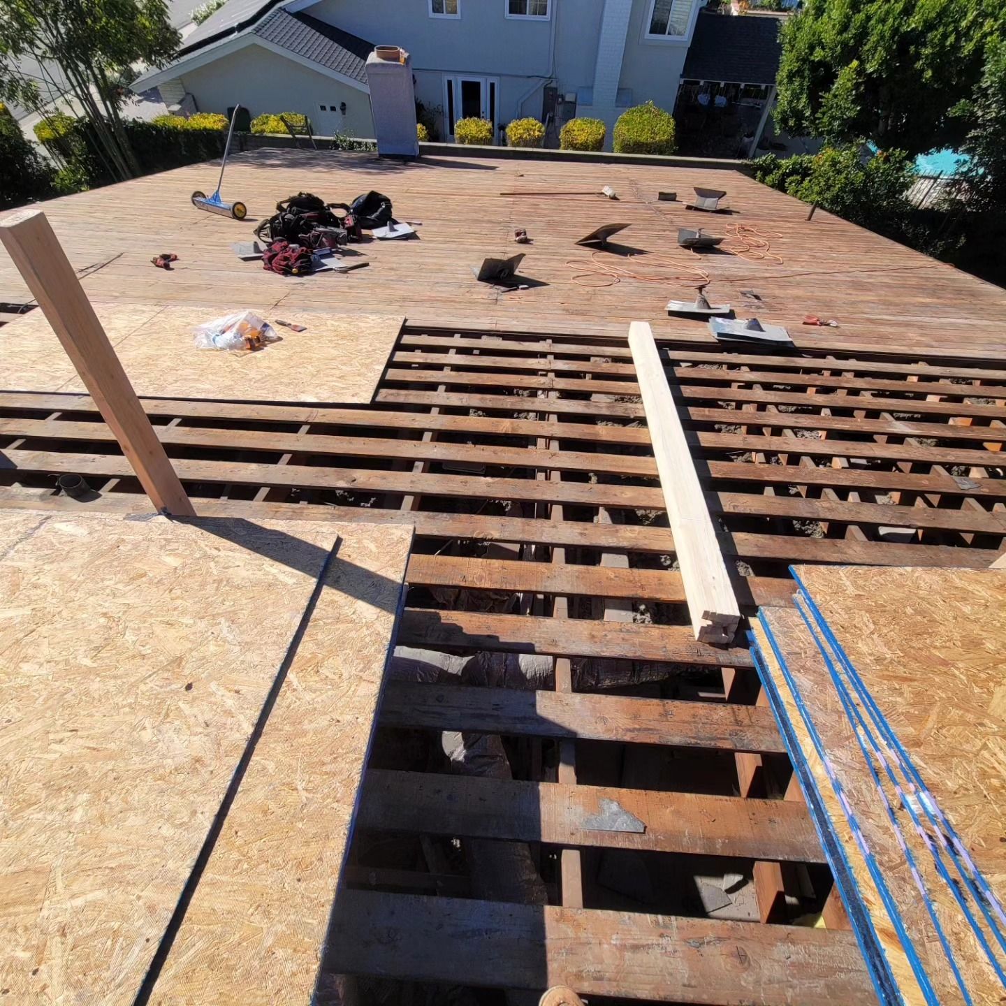 Roof deck under construction with exposed plywood, scattered tools, and blue safety lines.