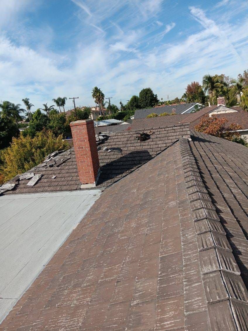 Rooftop with damaged shingles and a chimney under a blue sky