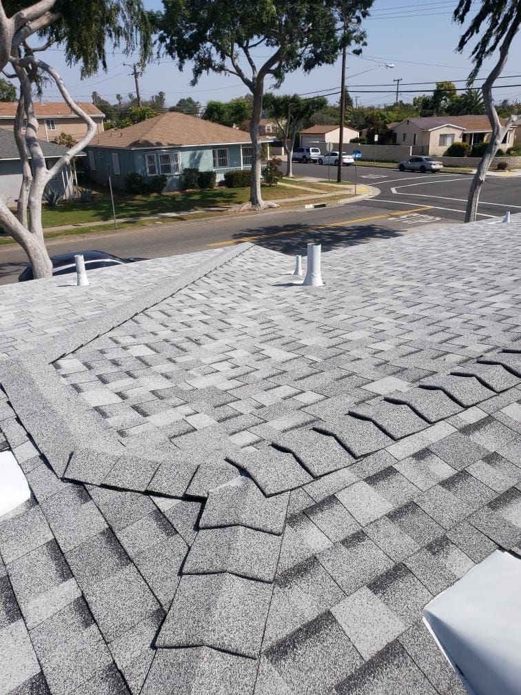 Shingled residential rooftop with vents, overlooking a quiet suburban street on a sunny day