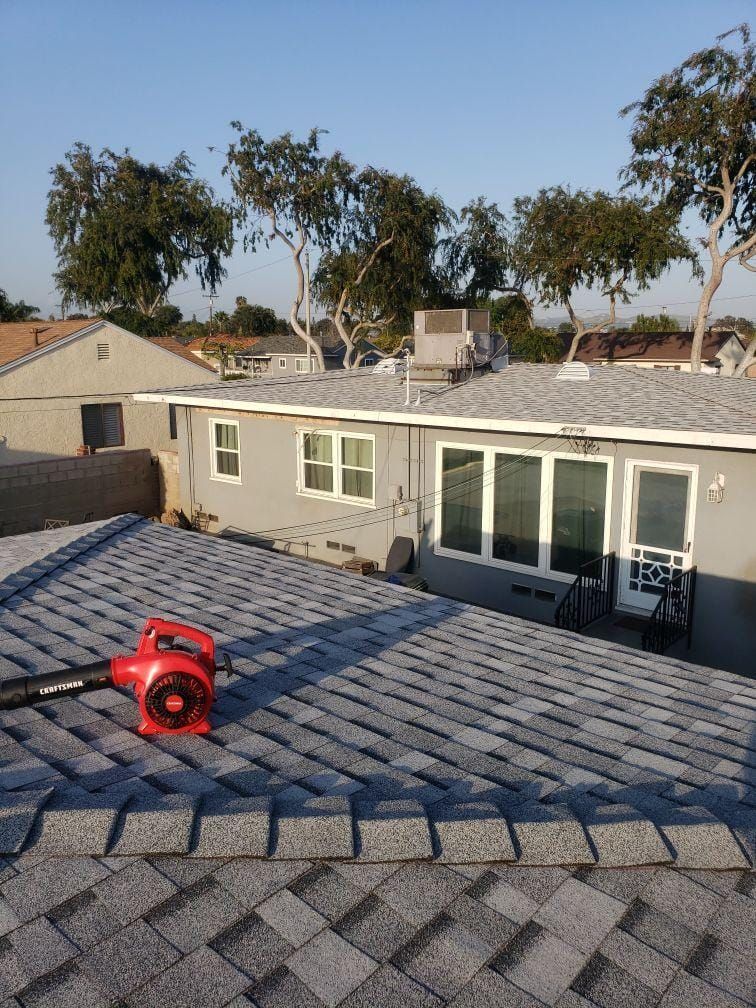 Rooftop view with a red tool on gray shingles, overlooking neighboring houses and trees.