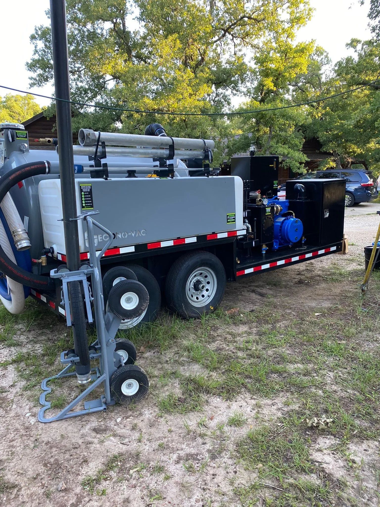 Utility trailer with industrial equipment and hoses parked on grass near trees.