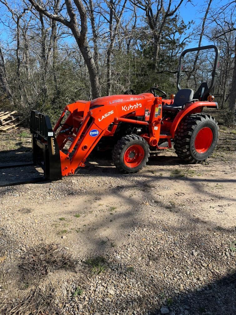 A red tractor with a forklift attached to it is parked on a dirt road.