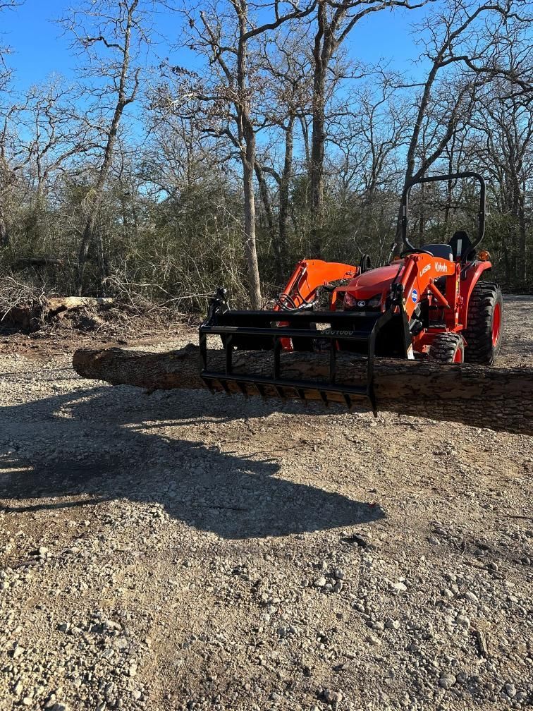 A tractor is carrying a large log in a gravel lot.