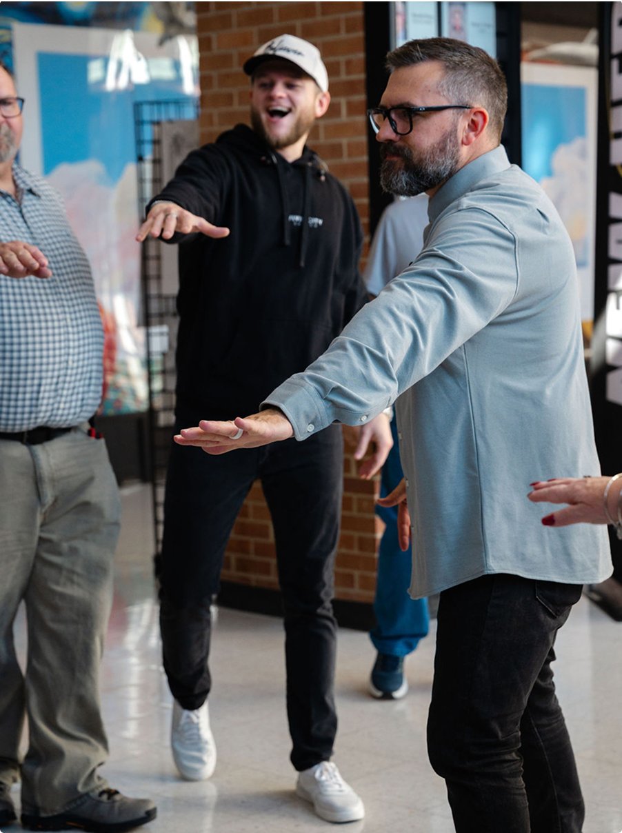 Three people indoors, smiling and gesturing with their hands in a casual conversation.