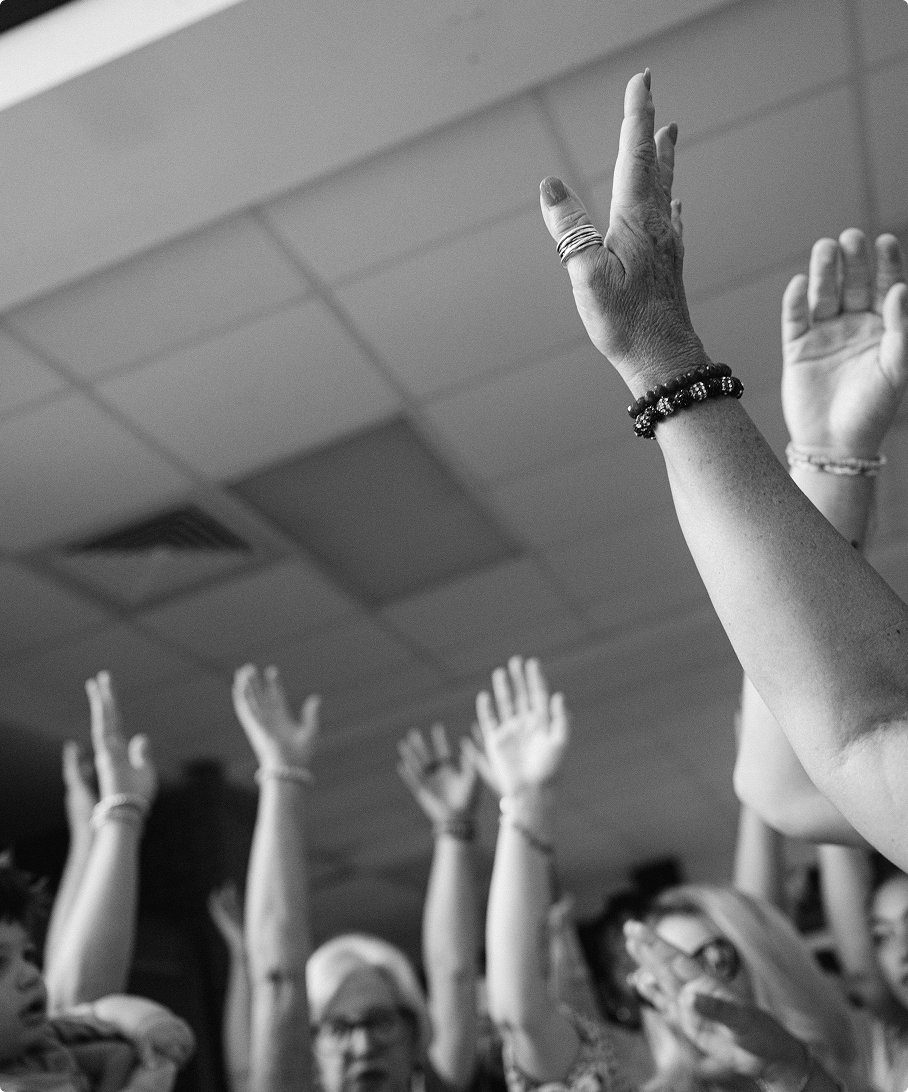 People in a room with raised hands, likely participating in a discussion or vote