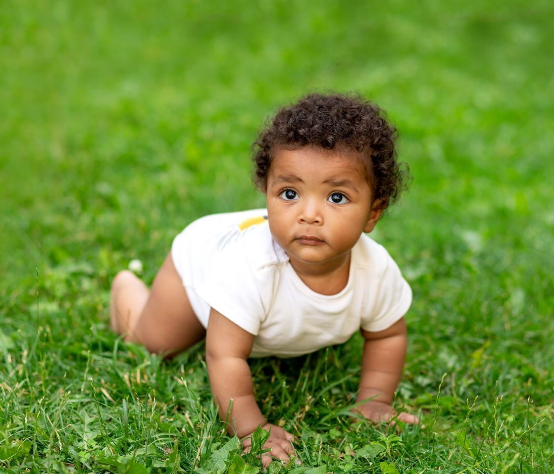 Small baby crawling on green grass.