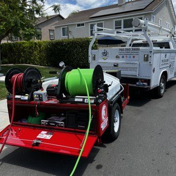 A red trailer with a green hose attached to it is parked next to a white truck.
