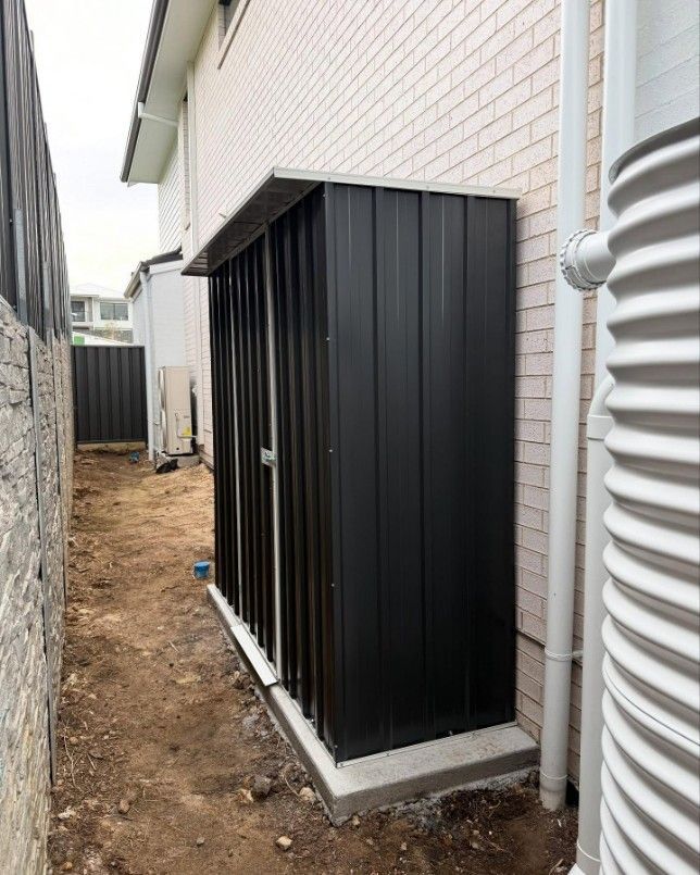A Black Shed is Sitting on the Side of a Brick Building — JOA - Construction & Maintenance Pty Ltd in Albion Park, NSW
