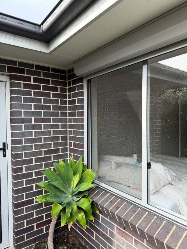 A Brick Building With a Window and a Plant in Front of It — JOA - Construction & Maintenance Pty Ltd in Albion Park, NSW