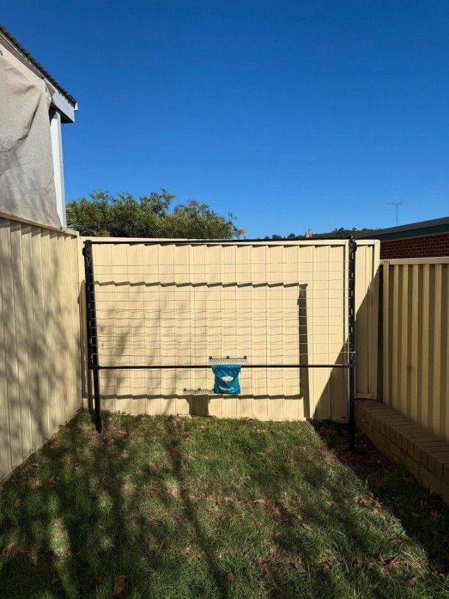 A Backyard With a Yellow Fence and a Blue Bucket in the Grass — JOA - Construction & Maintenance Pty Ltd in Narellan, NSW
