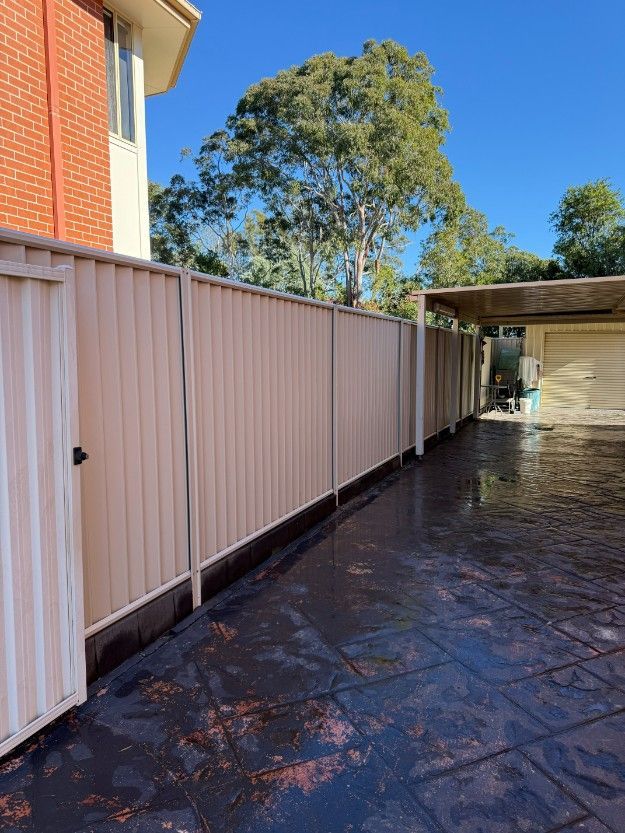 A White Fence Surrounds a Driveway in Front of a Brick House — JOA - Construction & Maintenance Pty Ltd in Appin, NSW