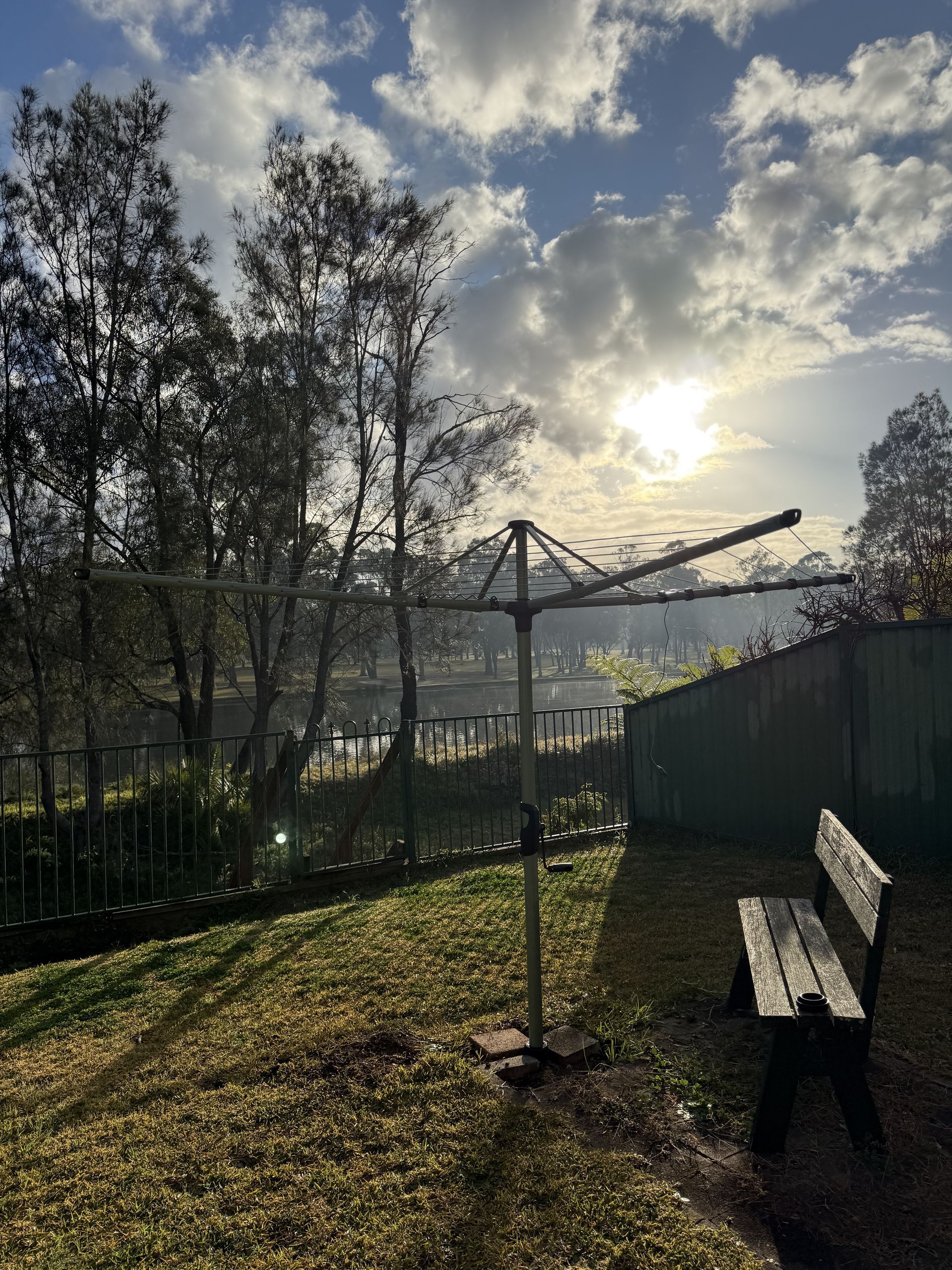 A wooden bench is sitting in the grass next to a clothes line. — JOA - Construction & Maintenance Pty Ltd in Campbelltown, NSW
