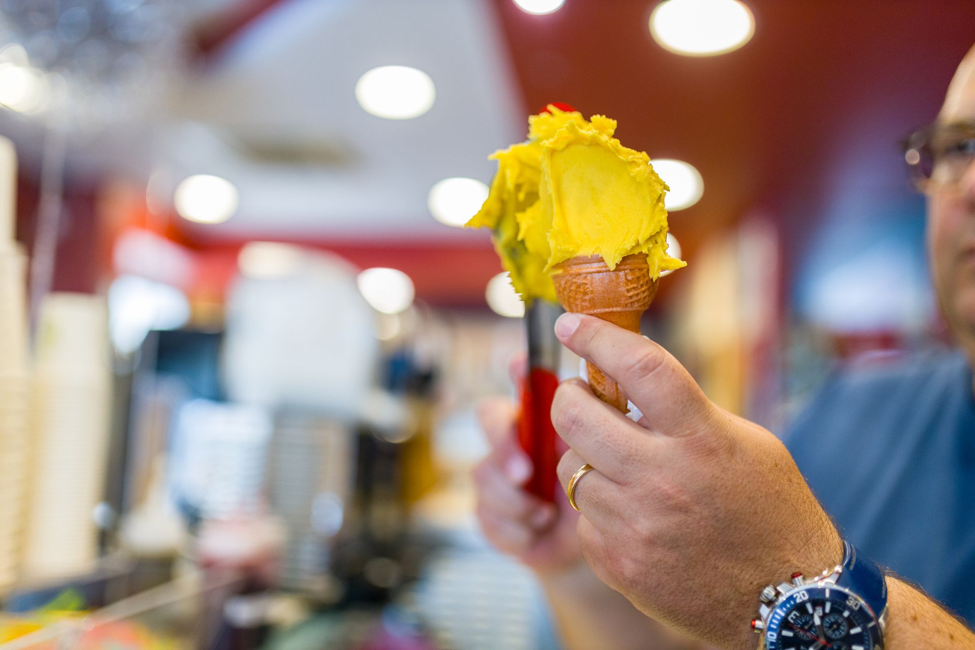 Mano che tiene un cono gelato giallo all'interno di un negozio luminoso