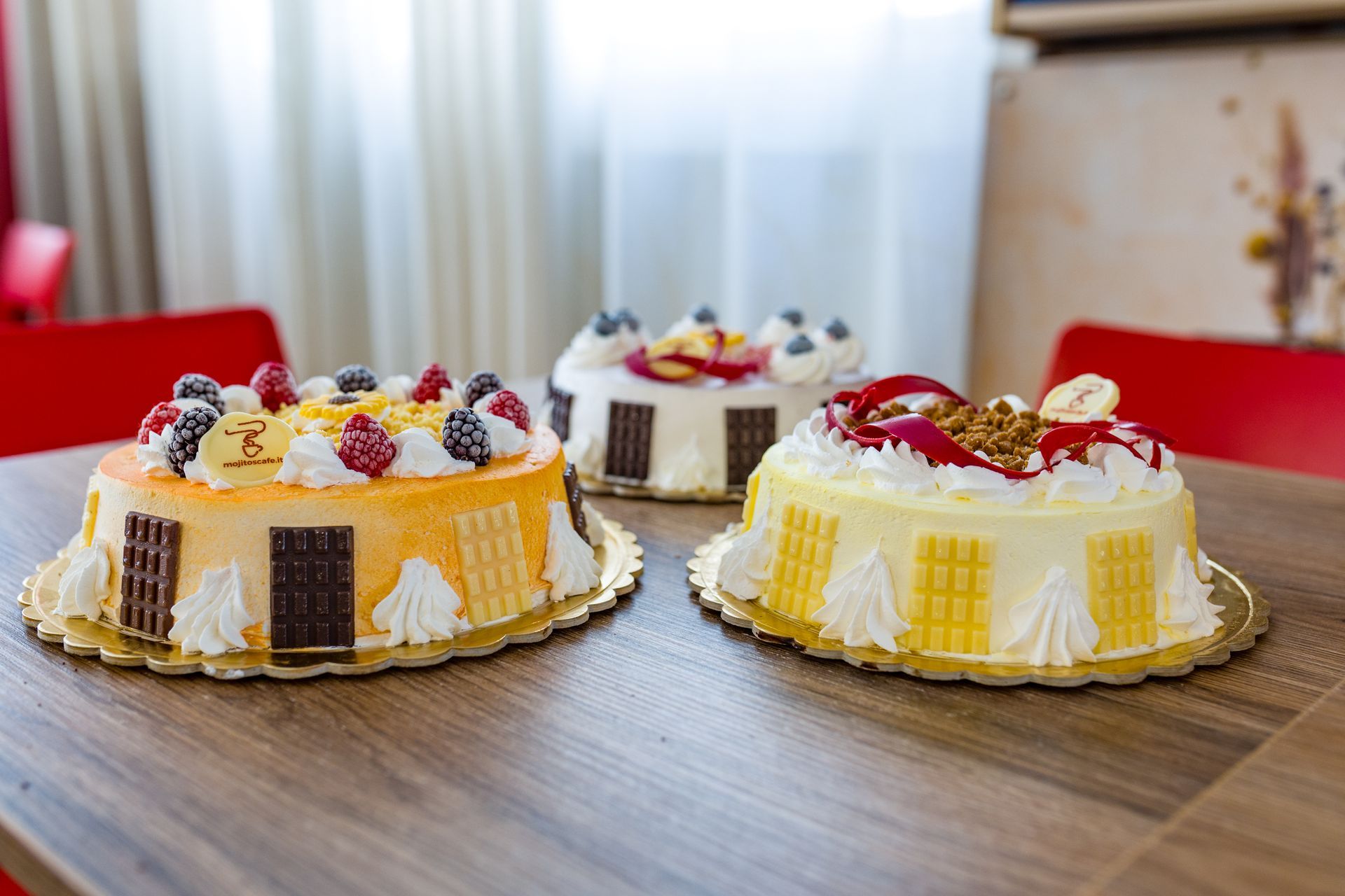 Tre torte decorate con frutti di bosco e panna su un tavolo di legno.