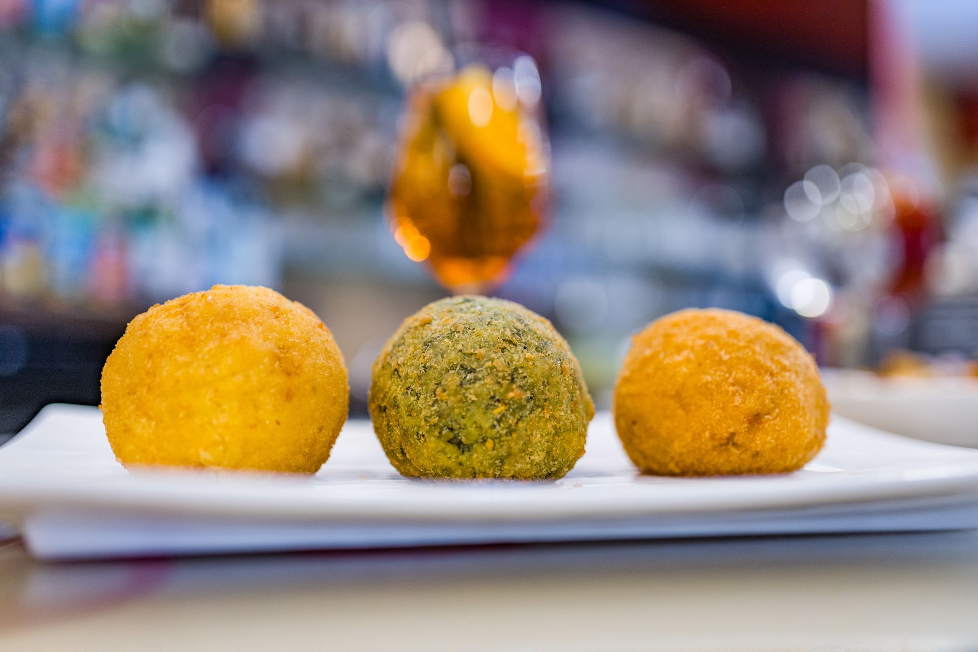 Tre colorate palline fritte su un piatto bianco, con uno sfondo sfocato.