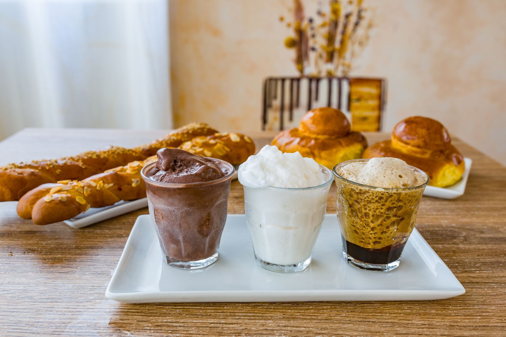 Dolci e bevande serviti su un tavolo di legno, tra cui caffè freddo e parfait con panna montata.