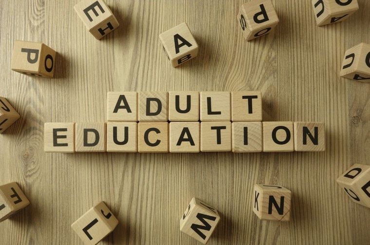 Wooden letter tiles spelling “ADULT EDUCATION” on a wood background