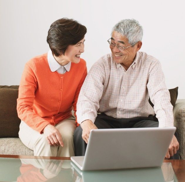 Two people smiling and chatting on a couch beside a laptop