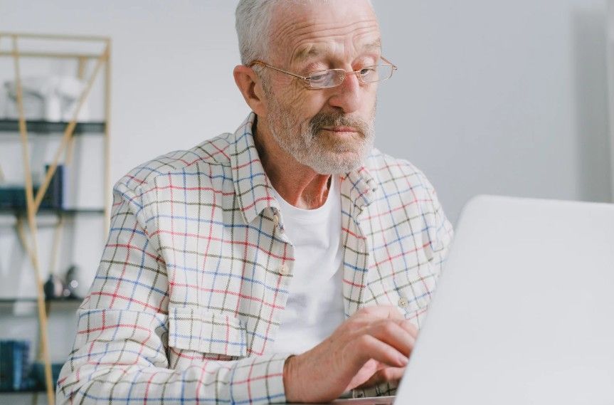 Older man typing on a laptop in a bright room