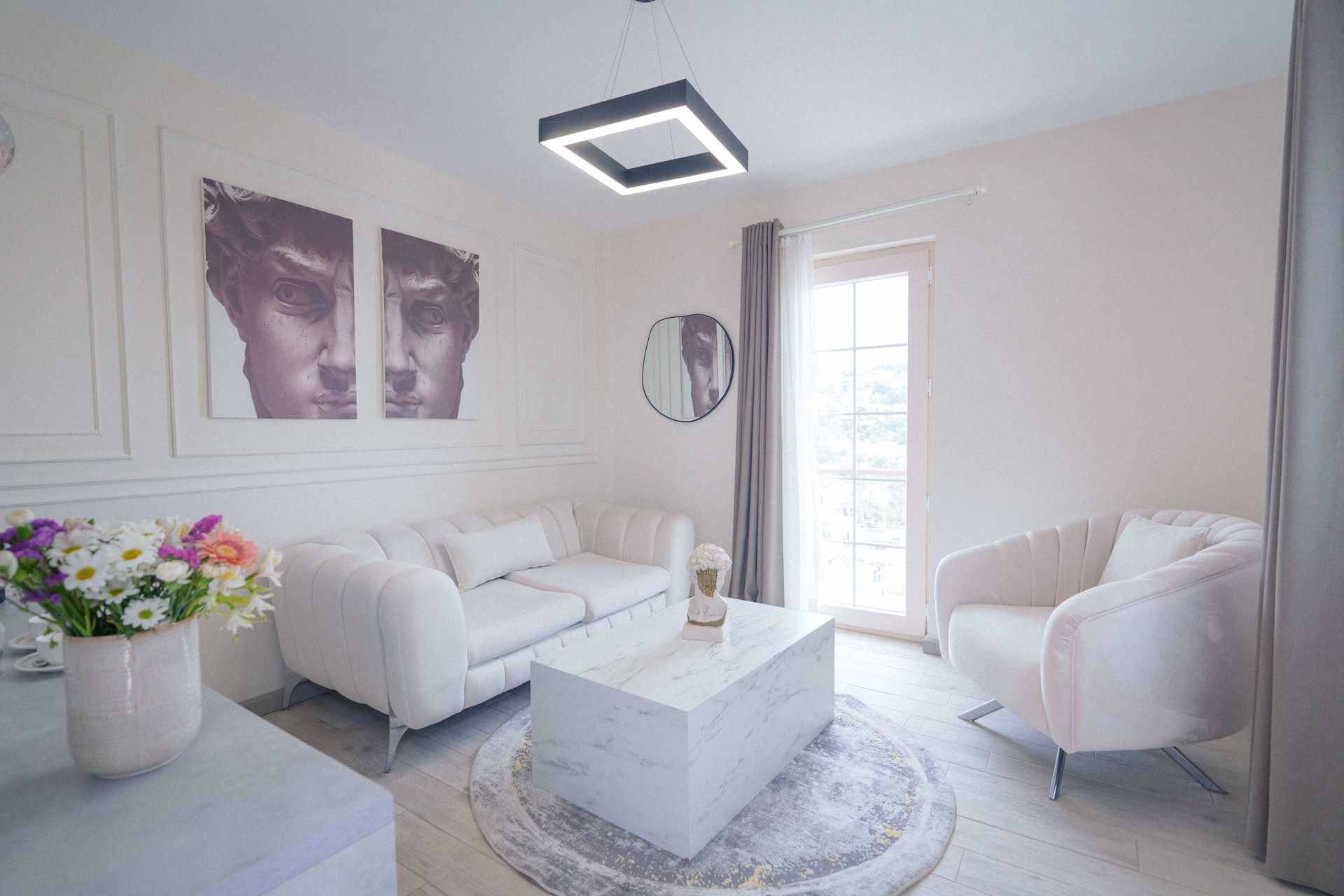 Elemanta Boutique Hotel | Bright white living room with sofa, armchair, coffee table, wall art, and a vase of flowers.