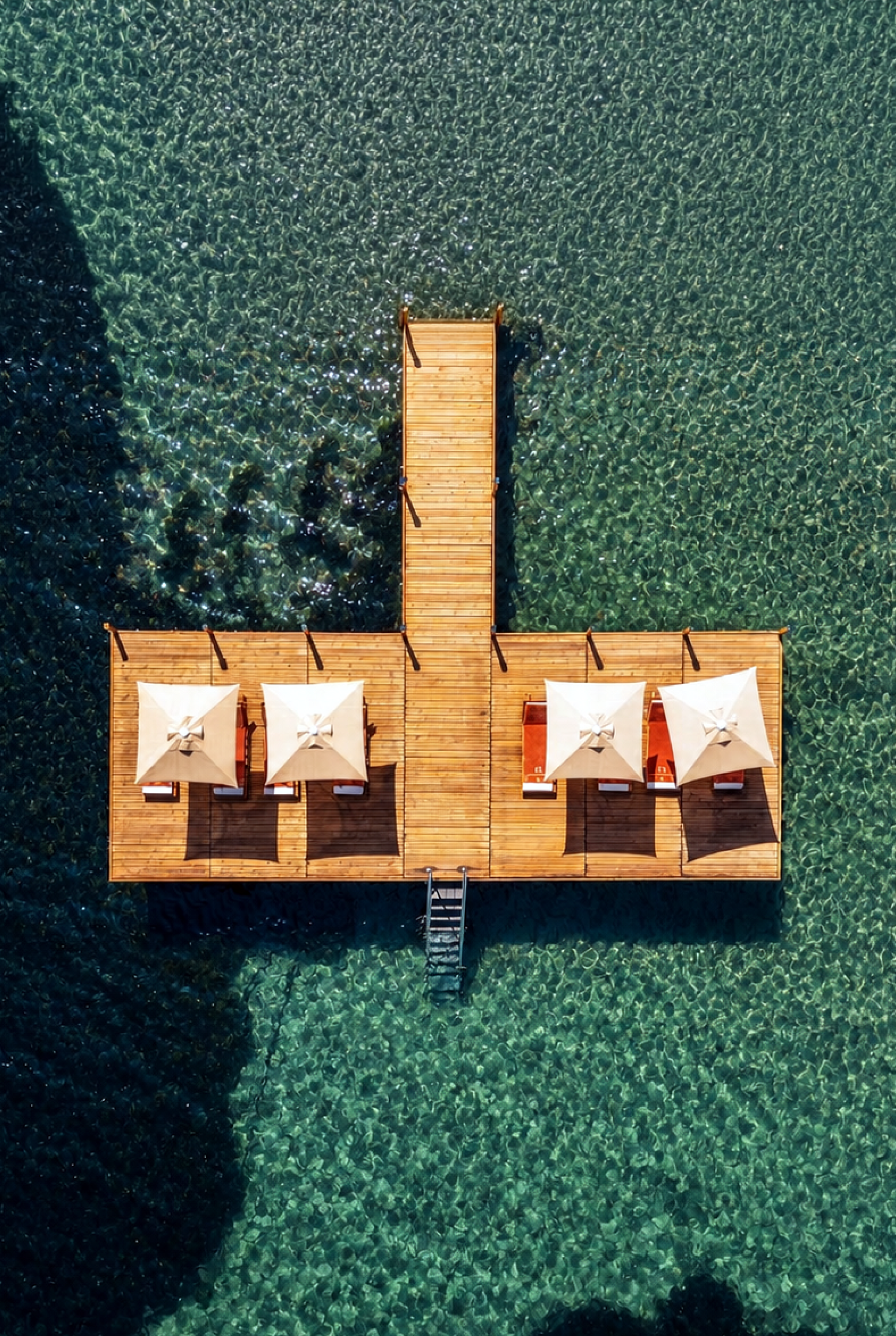 Elemanta Boutique Hotel | Wooden dock with four white lounge chairs extending into clear green water.