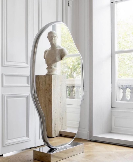 Elemanta Boutique Hotel | Tall oval mirror reflecting a white bust sculpture in a bright room with tall windows