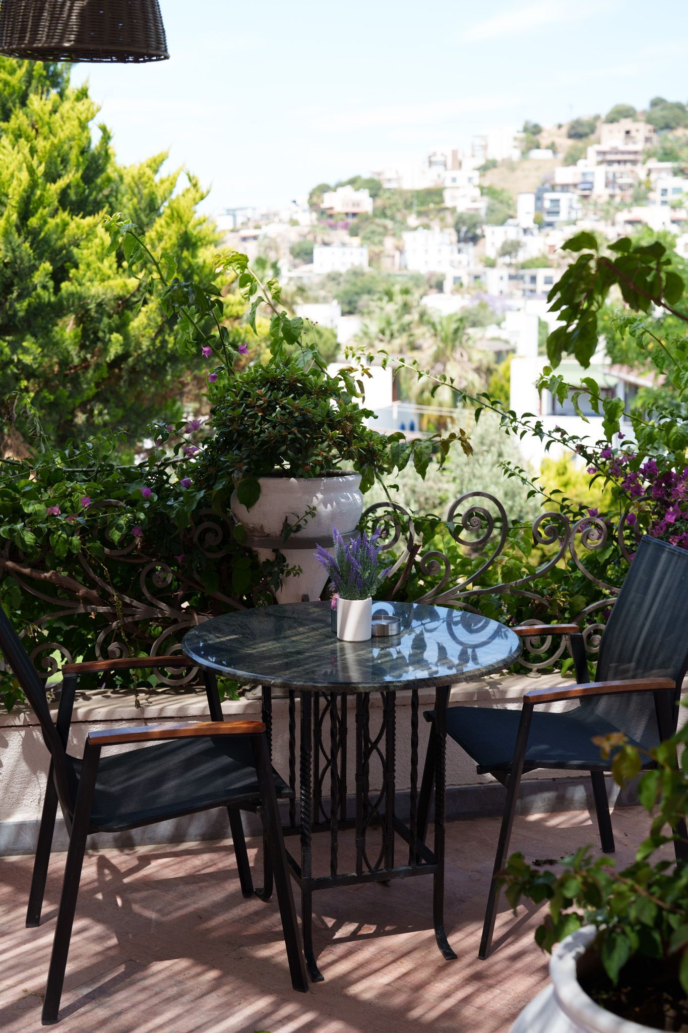 Elemanta Boutique Hotel |  Patio table and chairs surrounded by lush greenery, overlooking a sunlit hillside neighborhood