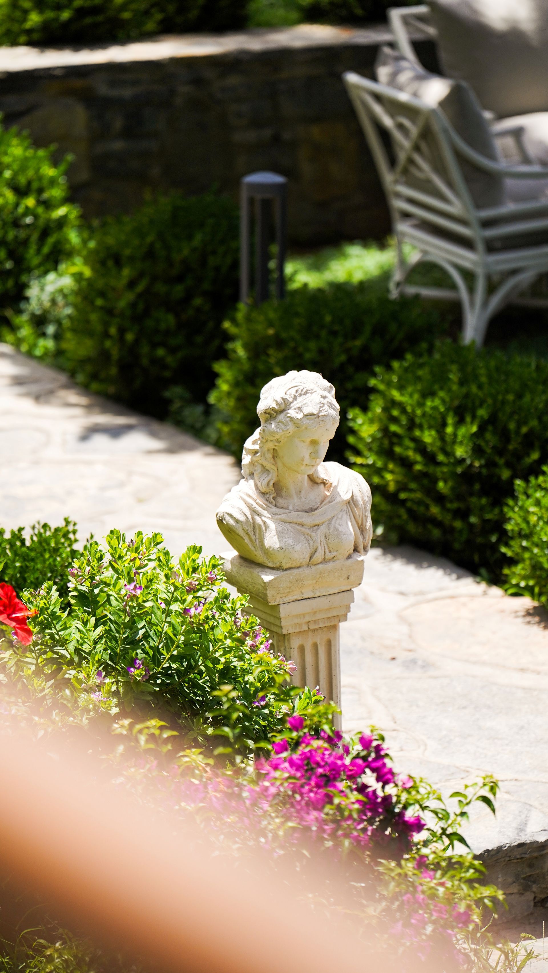  Elemanta Boutique Hotel |  Garden path with a white bust statue, pink flowers, and patio chairs in the background