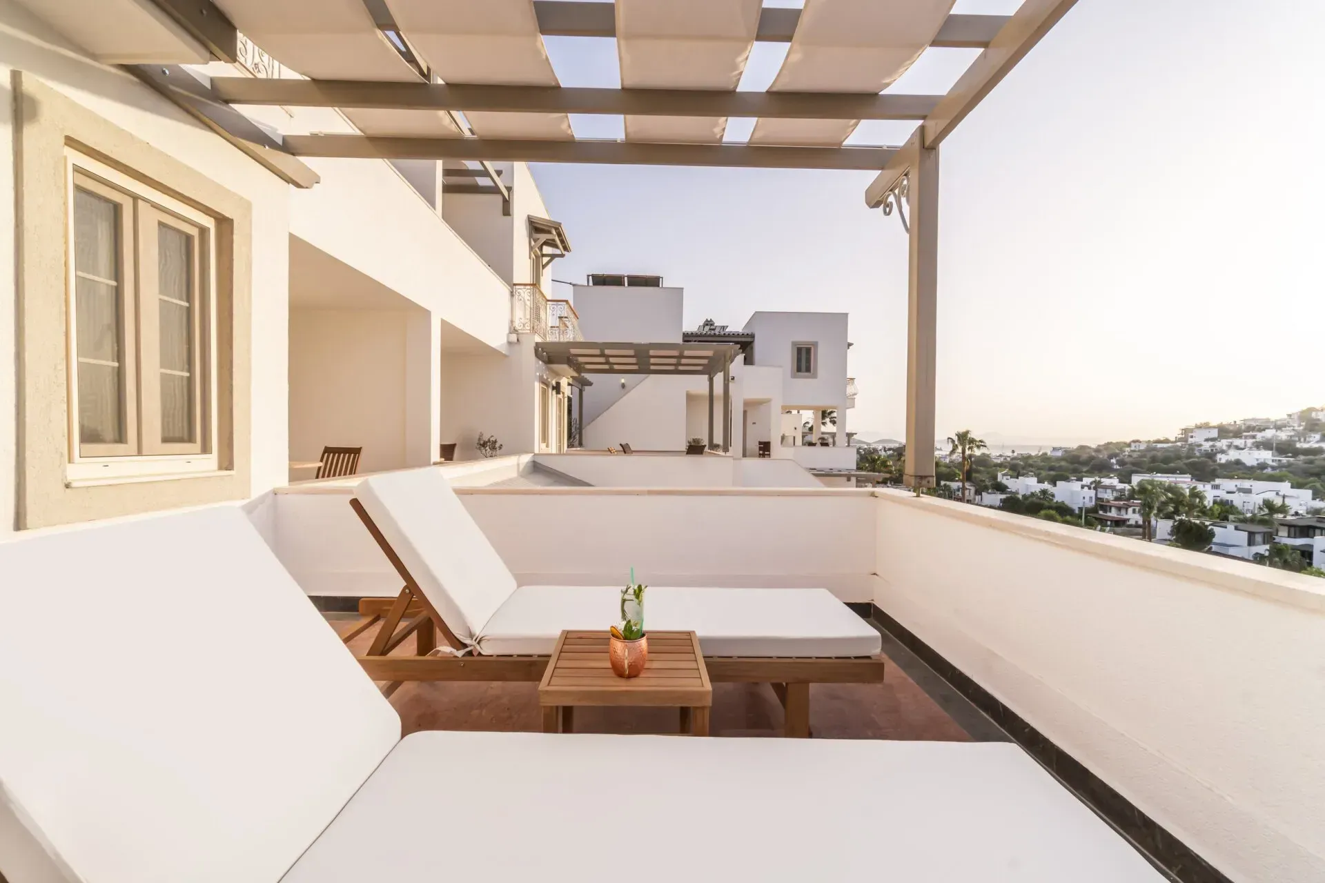  Elemanta Boutique Hotel | Sunny rooftop terrace with white lounge chairs, wooden table, pergola, and city view