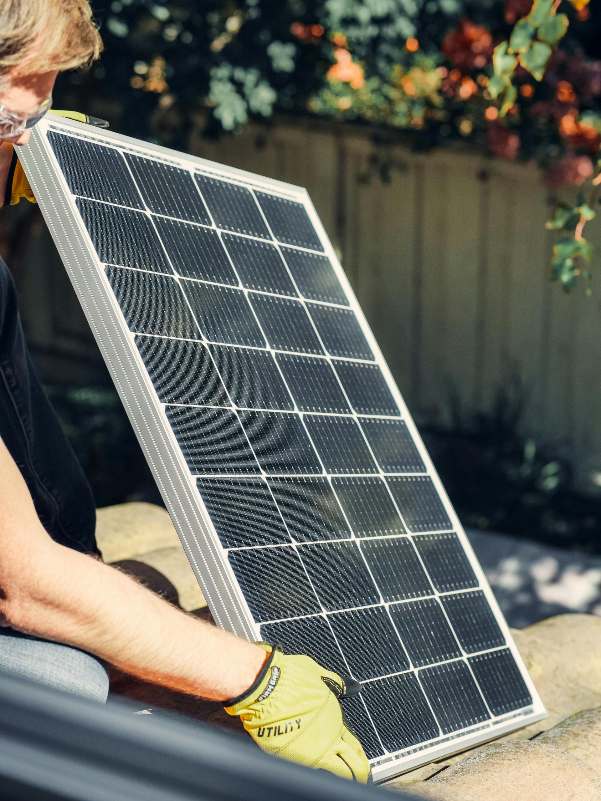 Elemanta Boutique Hotel | Person holding a solar panel outdoors, wearing yellow gloves, with a garden fence in the background