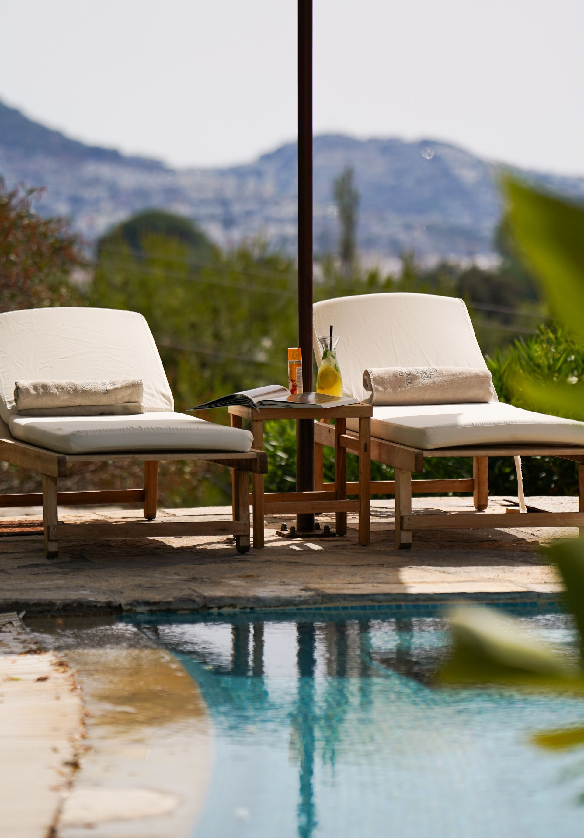 Elemanta Boutique Hotel |Two cushioned lounge chairs by a pool with a small table and mountain view beyond