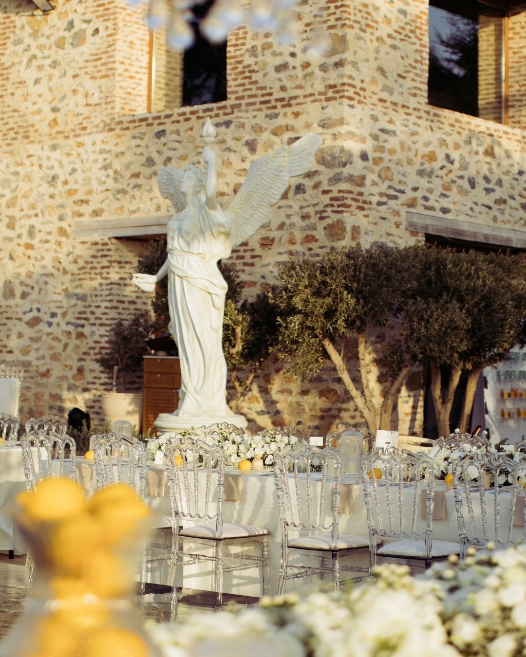 Elemanta Boutique Hotel | White angel statue amid clear chairs and flowers in an outdoor stone courtyard setting