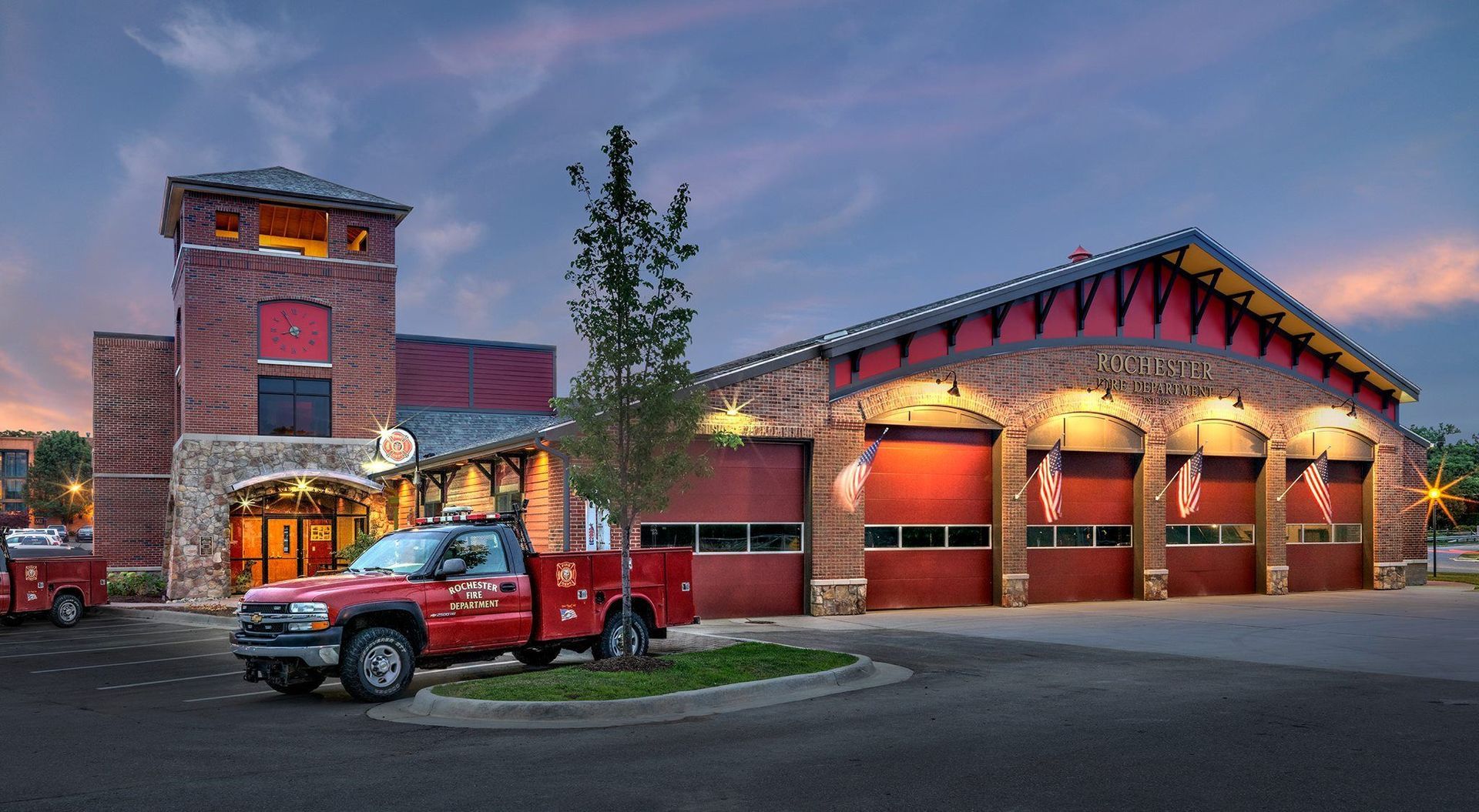Fire station with red trucks and illuminated garage bays at dusk